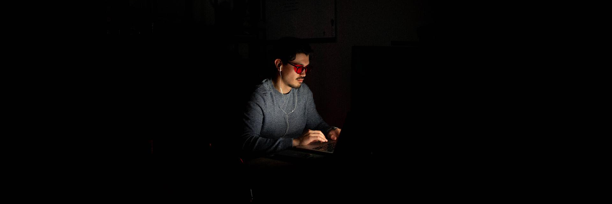 Person wearing red-tinted glasses while working on a laptop in a dark room