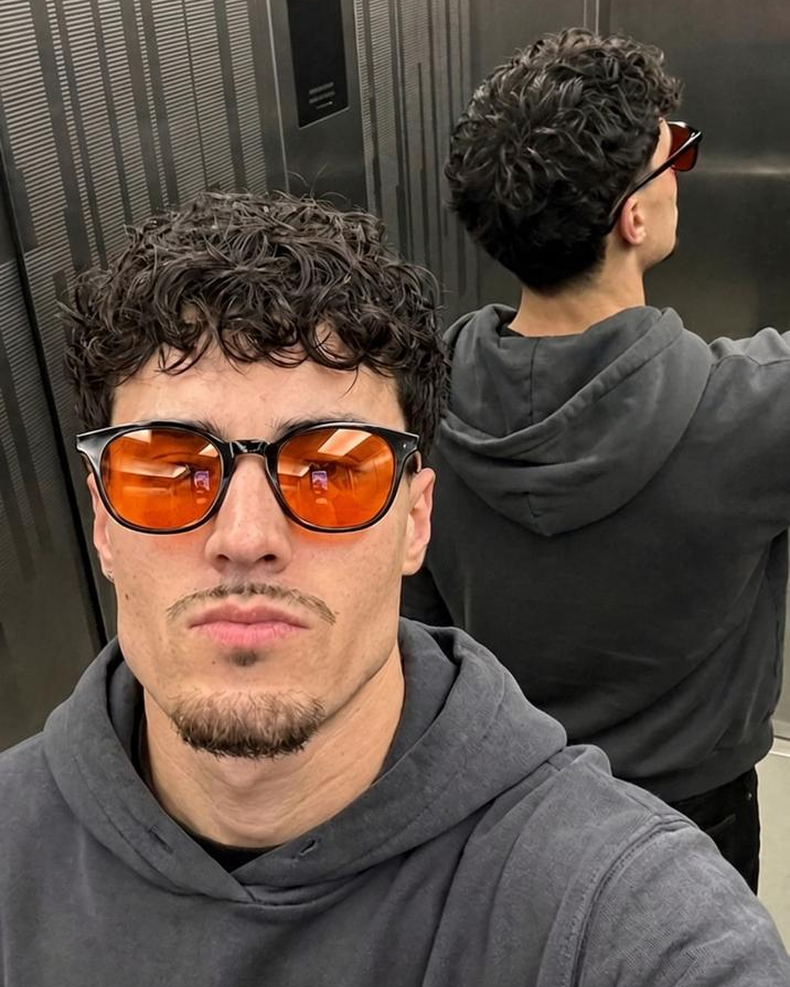Orange-lens glasses with a charcoal hoodie in an elevator portrait
